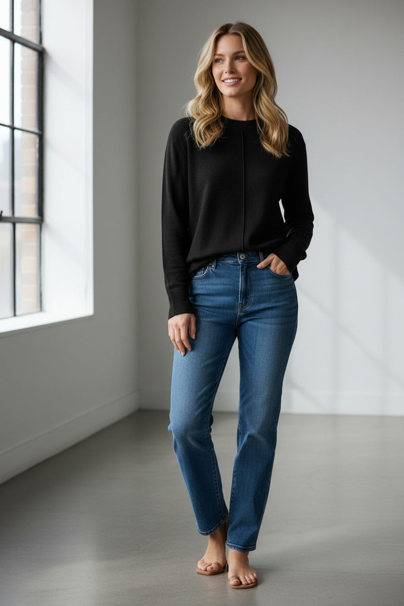 A person with long, light brown hair is wearing the KINROSS CASHMERE - HI LOW SEAMED CREW NECK CASHMERE SWEATER IN BLACK by KINROSS, styled in a relaxed classic fit with blue jeans. They are standing against a plain white background, facing the camera and smiling slightly.