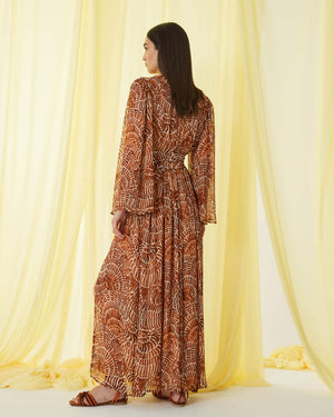 The SFIZIO - RUST PRINT RUFFLED DRESS by SFIZIO is a long, full-sleeved, flowy dress made in Italy, featuring a brown and beige spiral pattern. It boasts a V-neckline, ruffled detailing on the bodice, and an elastic waistband. Crafted from lightweight viscose creponne, it’s perfect for warm weather.