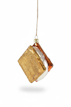 The CODY FOSTER S'MORE ORNAMENT features glittery gold graham crackers, a white marshmallow, and brown chocolate—hanging by a string, it's a perfect collectible or a thoughtful gift for design lovers.
