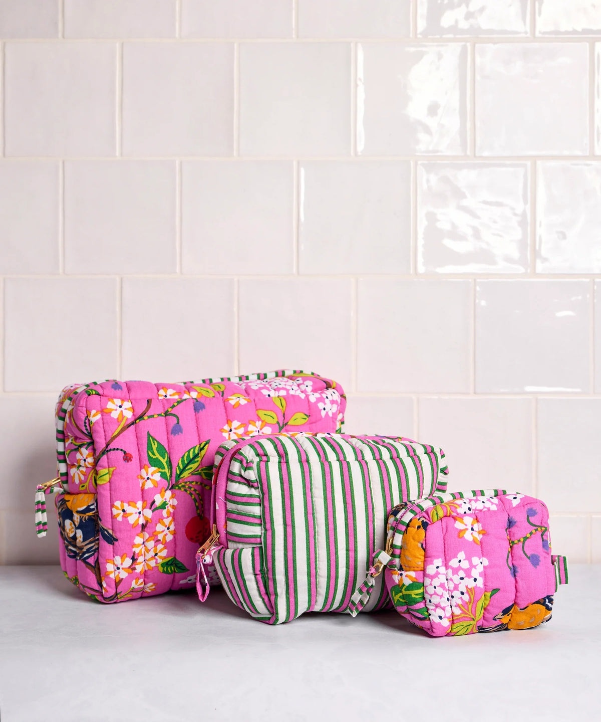 A person in a white shirt holds the PRINTFRESH - BIRD &amp; BLOSSOM THREE POUCH SET by PRINTFRESH, featuring three quilted makeup pouches with colorful floral and striped patterns, nested from smallest to largest.