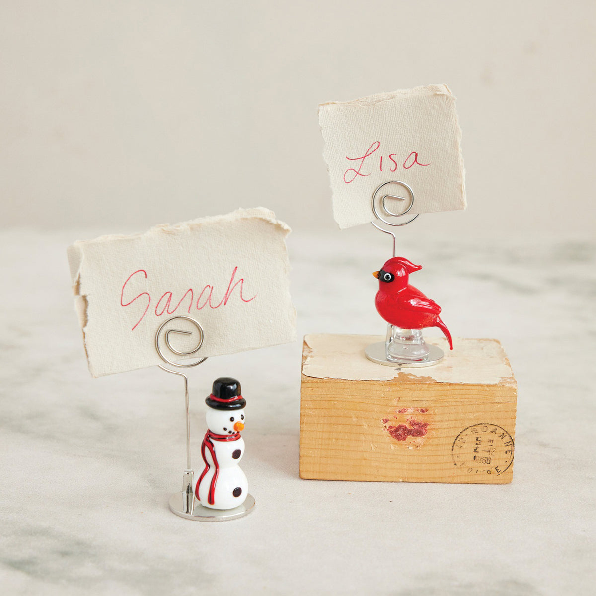 The CREATIVE COOP CARDINAL GLASS PLACECARD HOLDER features a red glass bird on a clear base with a spiral metal holder, perfect for displaying photos, notes, or place cards.
