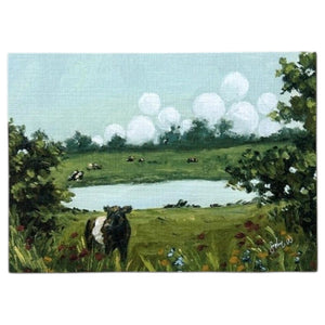 Bring the countryside to your home with the SOPHIE WYATT STUDIO - WILD MEADOWS & BELTIES ART PRINT (12x16). This fine art print by SOPHIE WYATT STUDIO depicts a serene scene where a Belted Galloway cow stands amid wildflowers beside a tranquil pond, while more cows graze in the distant field. Lush bushes frame the landscape and white fluffy clouds float across a vivid blue sky, perfectly capturing the peaceful charm of rural life.
