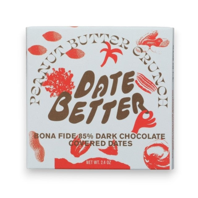 A white "DATE BETTER - PEANUT BUTTER CRUNCH COVERED DATES" package from DATE BETTER SNACKS rests on marble, cacao nibs and nuts spilling out. Orange text and illustrations adorn the packaging, adding charm to the scene.