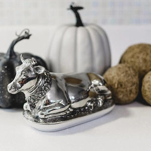 The VAGABOND HOUSE Mabel Cow Butter Dish, by VAGABOND HOUSE, is a silver-toned luxury pewter piece with intricate details. The cow’s textured features and elegant oval base highlight its exquisite craftsmanship.