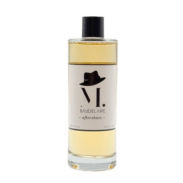 A clear bottle filled with yellow liquid, BAUDELAIRE - M.B. AFTERSHAVE by BAUDELAIRE features a classic design with a black hat graphic on the front and a black cap, offering a refreshing green-forest scent enriched with soothing witch hazel.