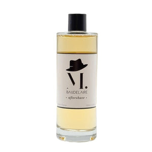 A clear bottle filled with yellow liquid, BAUDELAIRE - M.B. AFTERSHAVE by BAUDELAIRE features a classic design with a black hat graphic on the front and a black cap, offering a refreshing green-forest scent enriched with soothing witch hazel.