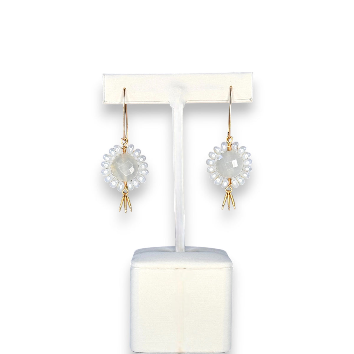 The GOLDISH - Floral Gemstone Earrings in Moonstone and White Pearl feature a circular, faceted moonstone center surrounded by white pearls, with three gold danglers, all set in 14K gold fill. Displayed on a white stand against a dark background.