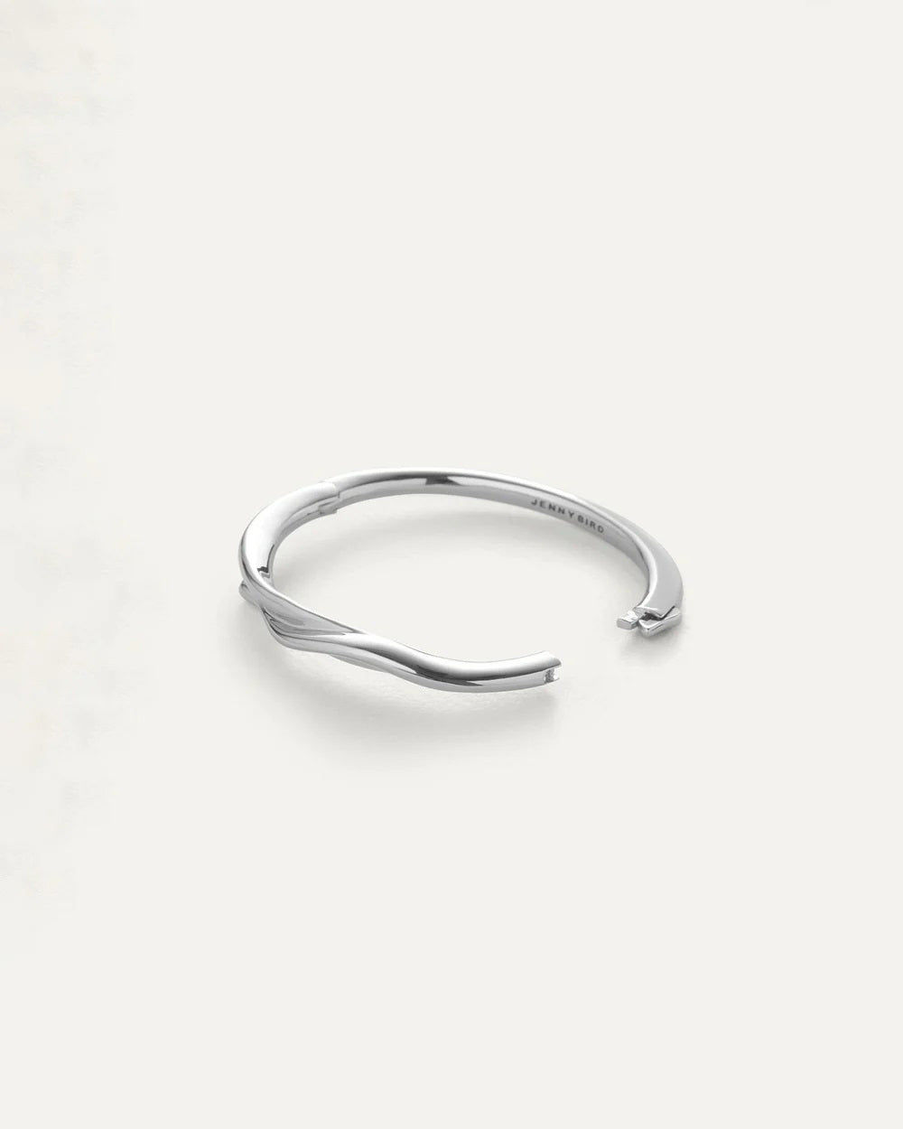 The JENNY BIRD COLETTE BANGLE, a sleek silver accessory with a subtle twist design and high-polish finish, is displayed on a light background.