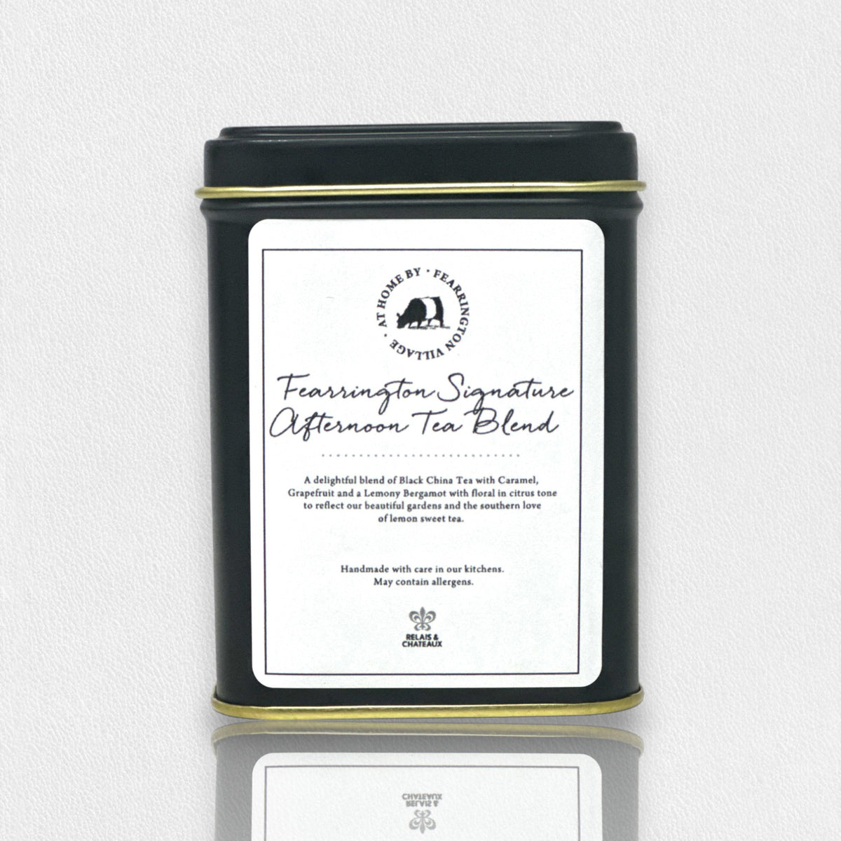 A black tin labeled &quot;Fearrington Signature Afternoon Tea Tin&quot; from the Fearrington House Signature Collection contains a luxurious blend of Loose Leaf Black China Tea with caramel, grapefruit, and lavender. The tin has a simple, elegant design accented by a white label featuring the product description.