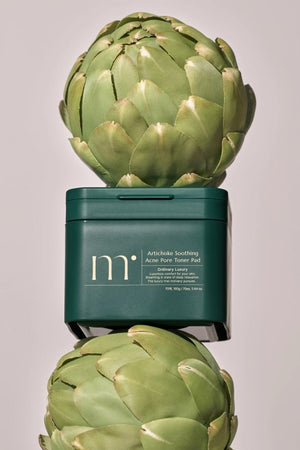 A dark green square container with a lid, labeled "MOLVANY - Artichoke Soothing Affect Pore Toner Pads" by HONG CHEON USA, INC. Tailored for acne-prone skin, this "ordinary luxury" item provides comfortable and luxurious care for sensitive skin.