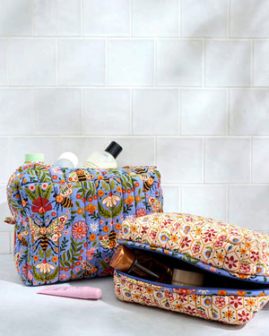 The PRINTFRESH Bee Tapestry Oversized Pouch Duo in Delphinium Blue features two quilted makeup pouches: the larger pouch showcases a blue bee and floral print, while the smaller pouch displays a cream background with red, yellow, and blue geometric shapes. Both PRINTFRESH bags are displayed on a tiled surface.