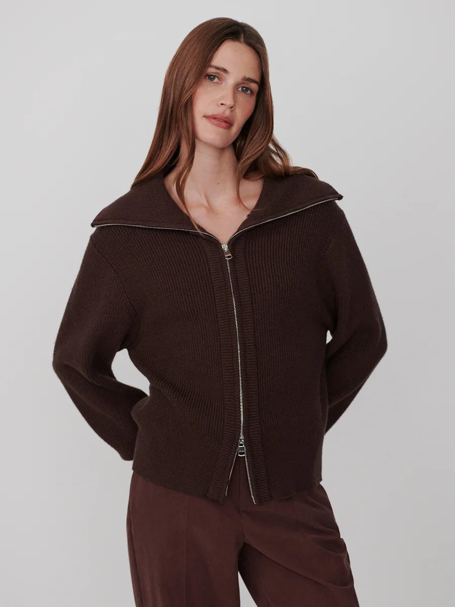 A person wearing a dark brown VARLEY - ENRICO ZIP-THROUGH KNIT JACKET featuring a ribbed soft viscose knit, a high collar, and a front zipper, ideal for cool weather layering.