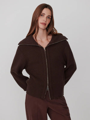 A person wearing a dark brown VARLEY - ENRICO ZIP-THROUGH KNIT JACKET featuring a ribbed soft viscose knit, a high collar, and a front zipper, ideal for cool weather layering.