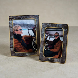 A person wearing sunglasses and a brown coat sits in a vintage car, holding the steering wheel. The photo is displayed in the ZODAX Marbled Hazel Resin Frame with Antique Brass Trim (4x6), featuring gold accents.