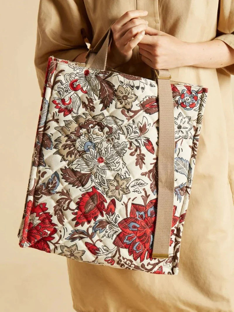 The INOUI EDITIONS - PIPPA STREET BAG by INOUI, a rectangular 100% cotton quilted crossbody tote with beige handles and a strap, is displayed against a plain background. The 40x34x12 cm bag showcases a colorful floral pattern featuring red, blue, and brown flowers on a light background.