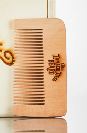 Four THE IMMACULATE BEARD - WOODEN BEARD COMBS stand upright in a small round black and brown ceramic bowl. Each laser-engraved comb by THE IMMACULATE BEARD features fine teeth and engraved text, ideal for beard grooming. Plain white background.