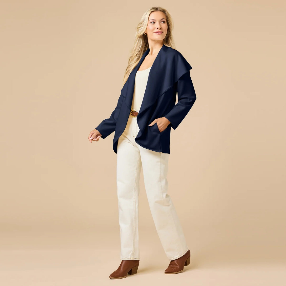 A woman wears an off-white SOFTIES - DREAMTECH EXAGGERATED COLLAR CARDIGAN with an exaggerated waterfall collar, cinched at the waist with a thin belt, and holds a matching handbag.