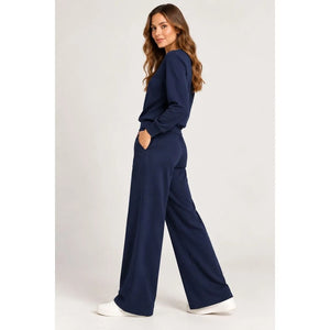 A woman wears a SOFTIES - DREAMTECH BOAT NECK WITH PINTUCK PANT SET in olive green, featuring a long-sleeve boat neck top and matching wide-leg pintuck pants.