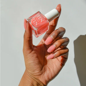 A glass bottle of TENOVERTEN - NAIL POLISH from the brand TEN OVER TEN, featuring a white cap and a dusty pink nail color. The front label displays "TEN OVER TEN" in white uppercase letters. This vegan, eight-free formula ensures both beauty and peace of mind. The background is plain and light-colored.