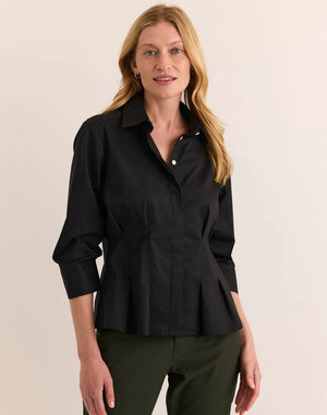 A woman with blonde hair is smiling at the camera while standing against a plain light background, wearing the HINSON WU - MARTINA 3/4 SLEEVE STRETCH POLISHED COTTON SHIRT IN BLACK paired with olive green pants.
