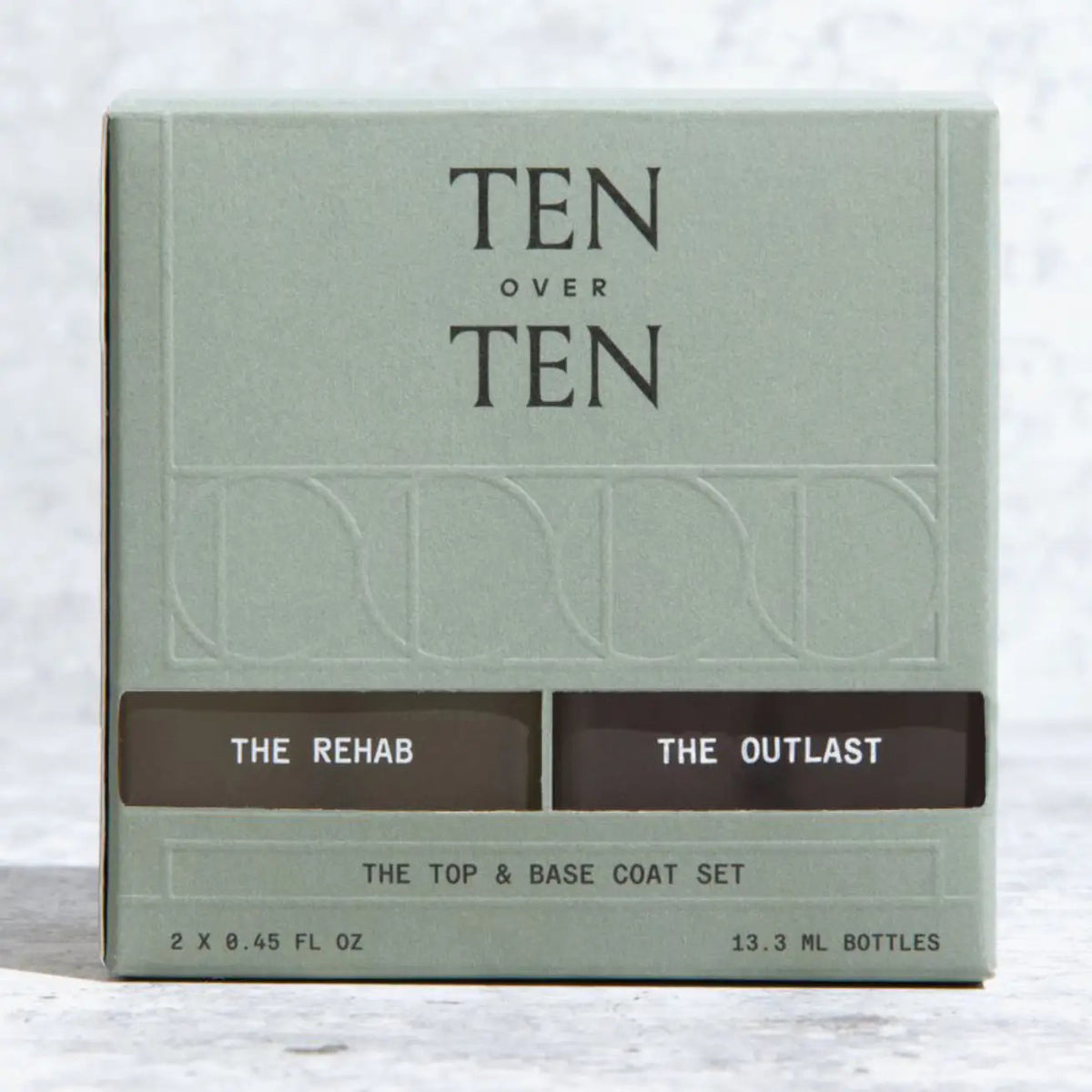 The TEN OVER TEN - THE REHAB TOP AND BASE COAT NAIL POLISH SET features two square glass bottles with white caps—one pale yellow (“REHAB” base coat) and one light purple (“THE OUTLAST” top coat)—side by side on a white background.