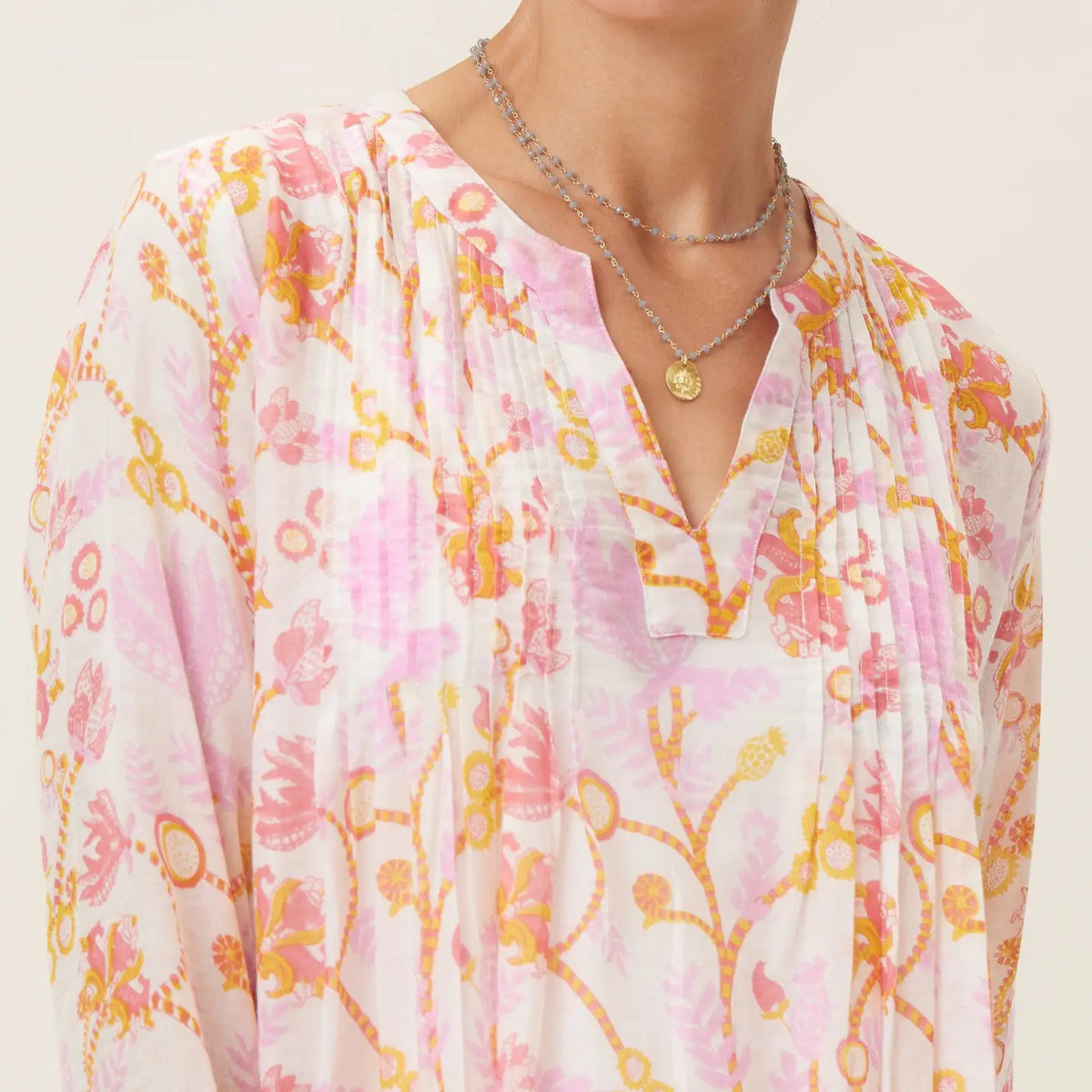 A woman with curly hair smiles wearing the ROCKFLOWERPAPER Gemma Pink Pintuck Beach Cover Up, a lightweight cover-up featuring a pink and orange floral pattern on a white background.