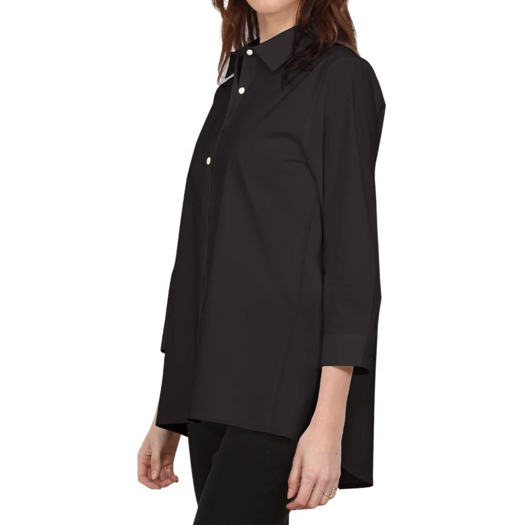 Sporting long hair, the individual is clad in a white HINSON WU - AILEEN TUNIC and black pants. The tunic-length shirt by Hinson Wu features a collar and two buttons near the top. They stand in front of a light gray wall with white molding, with their face not visible in the image.