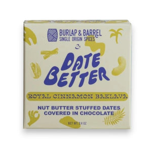 Two boxes of DATE BETTER - ROYAL CINNAMON BAKLAVA by DATE BETTER SNACKS, featuring nut butter-stuffed Medjool dates topped with chocolate, a cinnamon stick, cashews, and pistachios arranged against a green backdrop—the perfect gluten-free snack for any occasion.