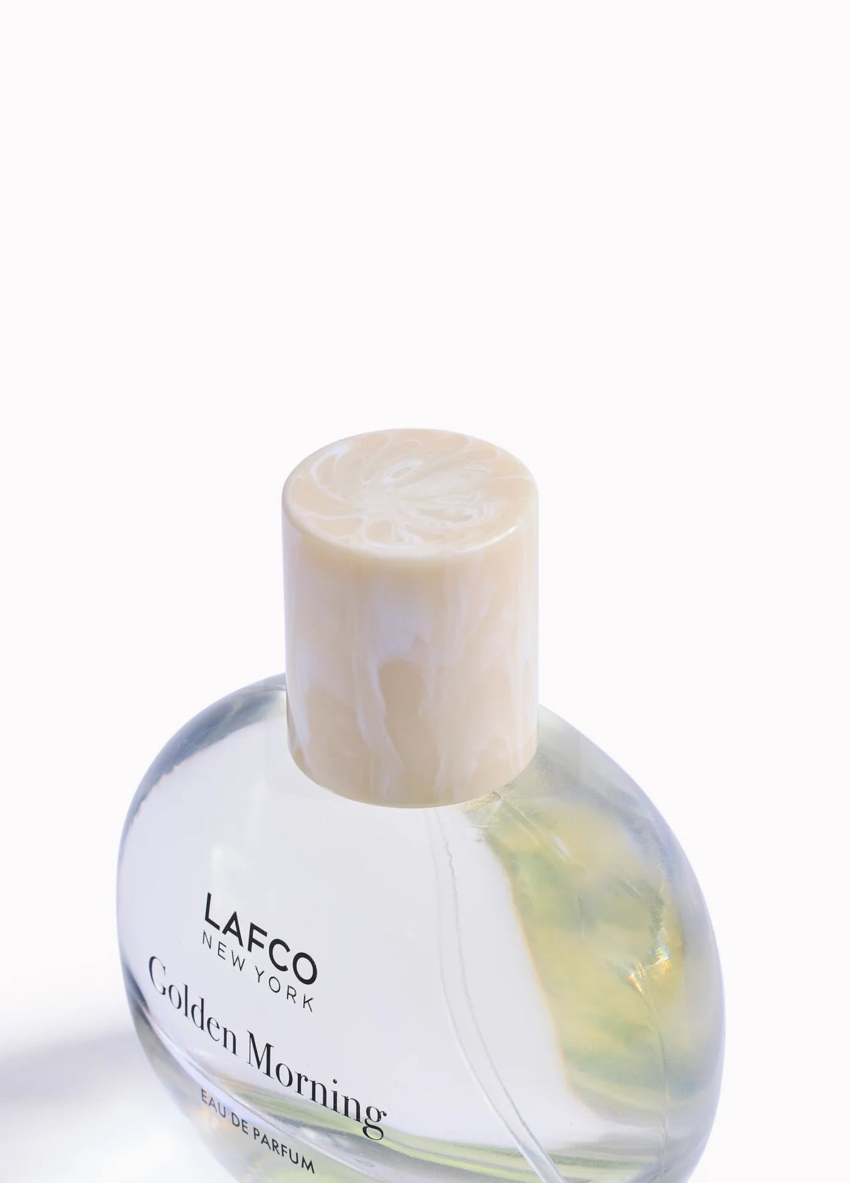 A transparent perfume bottle labeled “LAFCO - FINE FRAGRANCE, GOLDEN MORNING 50ML” by LAFCO features a round, marble-textured cream cap and is displayed against a plain white background. This floral scent is crafted as a vegan and cruelty-free fine fragrance, designed to deliver a sophisticated and conscious olfactory experience.
