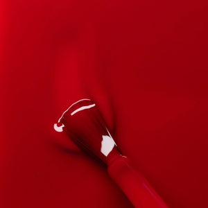 A close-up of the MANUCURIST - GREEN™ NAIL POLISH IN RED CHERRY brush, surrounded by glossy vegan polish from MANUCURIST INC, creating smooth ripples on the vibrant red surface.