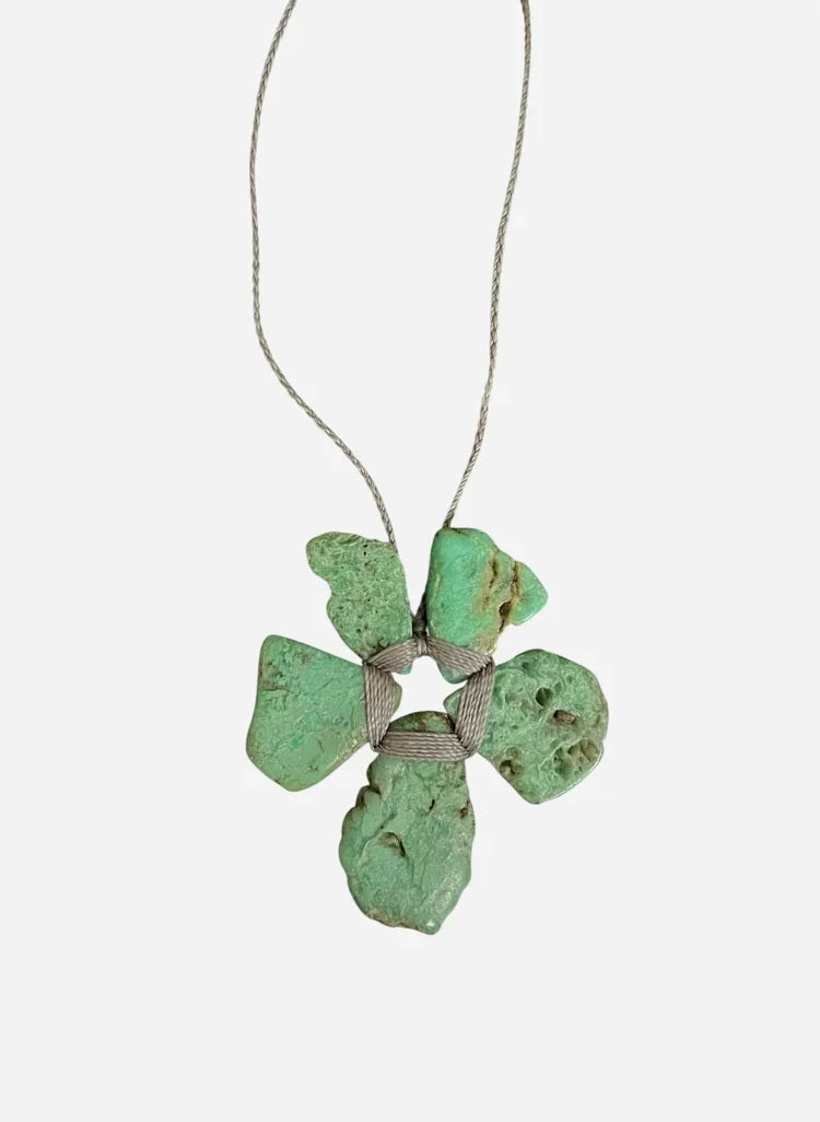 The ANN LIGHTFOOT - ROUGH CUT CHRYSOPRASE FLOWER NECKLACE by ANN LIGHTFOOT features four irregular green chrysoprase stones arranged in a flower-like shape, secured with wrapped cord and suspended from a delicate silver chain, shown against a white background.