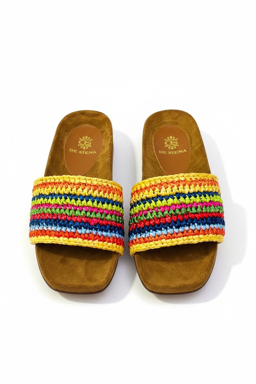 The DA SIENA - LUCILLA RAFIA SLIDE by DE SIENA features open-toe sandals with brown suede soles, a comfy eco footbed, wide multicolored woven straps in green, blue, yellow, and brown stripes, and a branded floral "DE SIENA" insole.