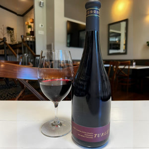 A dark glass wine bottle with a long neck and a black capsule on top features a black and maroon label reading “TURLEY.” Crafted by WINE: ADVINTAGE, this distinctive bottle contains their TURLEY ‘DEL BARBA’ ZINFANDEL 2023, renowned for its rich character and celebrated old vine heritage.