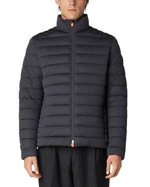 Someone stands against a plain white background wearing the SAVE THE DUCK - ARI PUFFER JACKET, a dark blue, quilted sustainable jacket by SAVE THE DUCK with a high collar and front zipper.