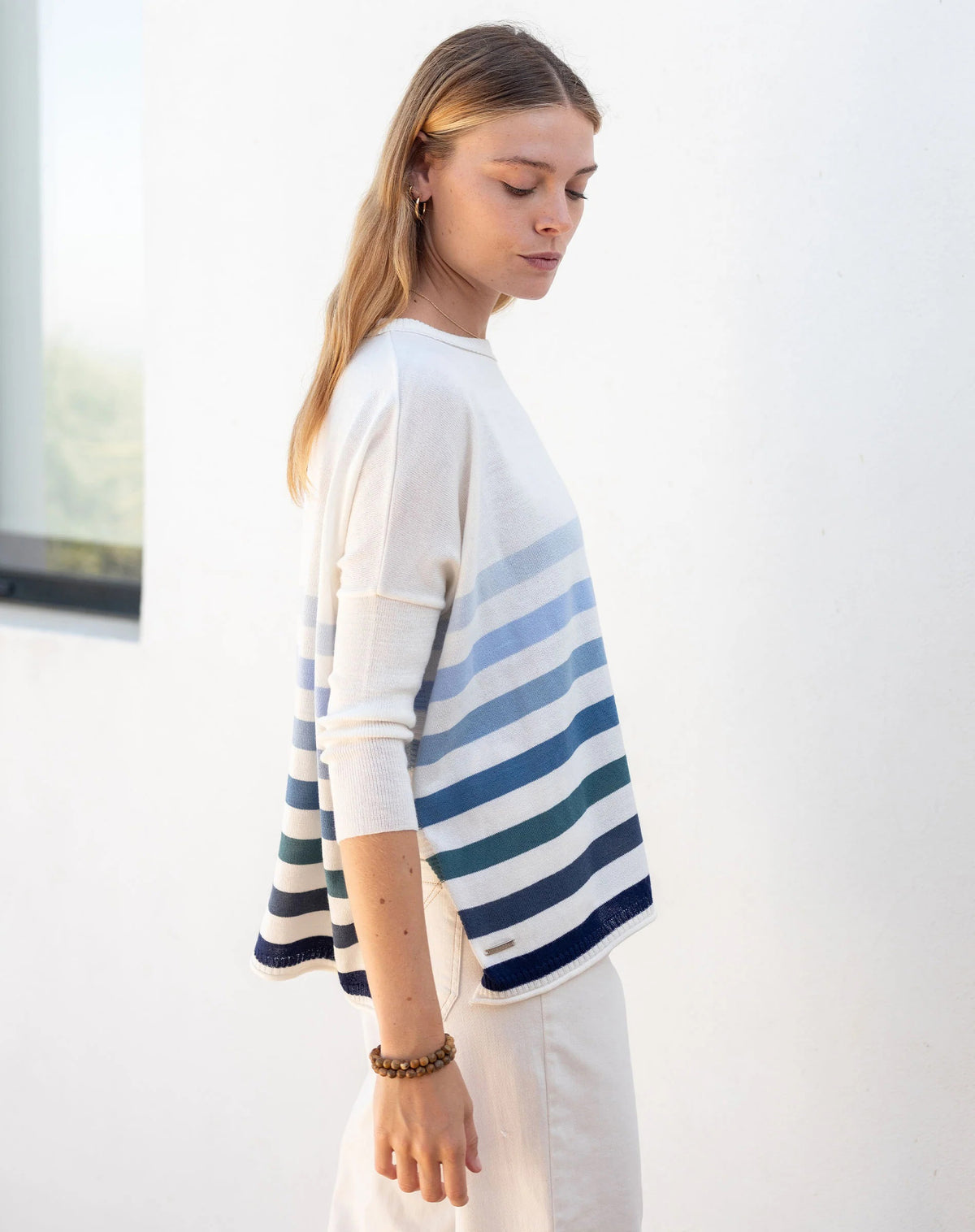 Woman wearing the MERSEA - CATALINA CREWNECK SWEATER, white with two black stripes, paired with denim shorts and a gold necklace—an essential piece from MERSEA for effortless, versatile style.