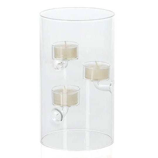 A SUSPENDED GLASS TEALIGHT HOLDER - LARGE by ZODAX holds several red-lit tealights, accented with pine branches and berries on a white surface, all set against a vibrant red background.