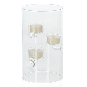 A SUSPENDED GLASS TEALIGHT HOLDER - LARGE by ZODAX holds several red-lit tealights, accented with pine branches and berries on a white surface, all set against a vibrant red background.