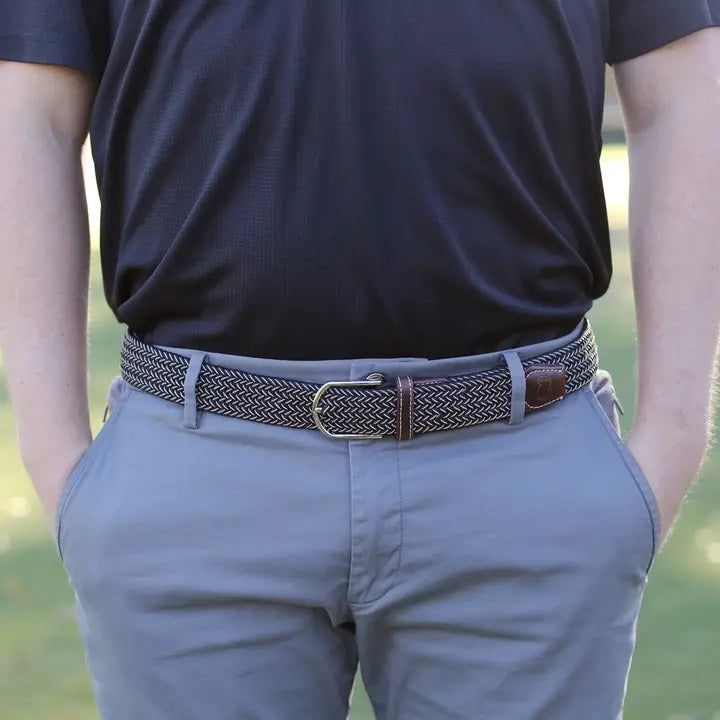 The ROOSTAS - MAUI WOVEN STRETCH BELT by ROOSTAS features a black and white zigzag pattern, brown leather ends, a silver buckle, and an adjustable clasp for the perfect fit.