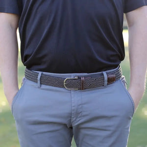The ROOSTAS - MAUI WOVEN STRETCH BELT by ROOSTAS features a black and white zigzag pattern, brown leather ends, a silver buckle, and an adjustable clasp for the perfect fit.