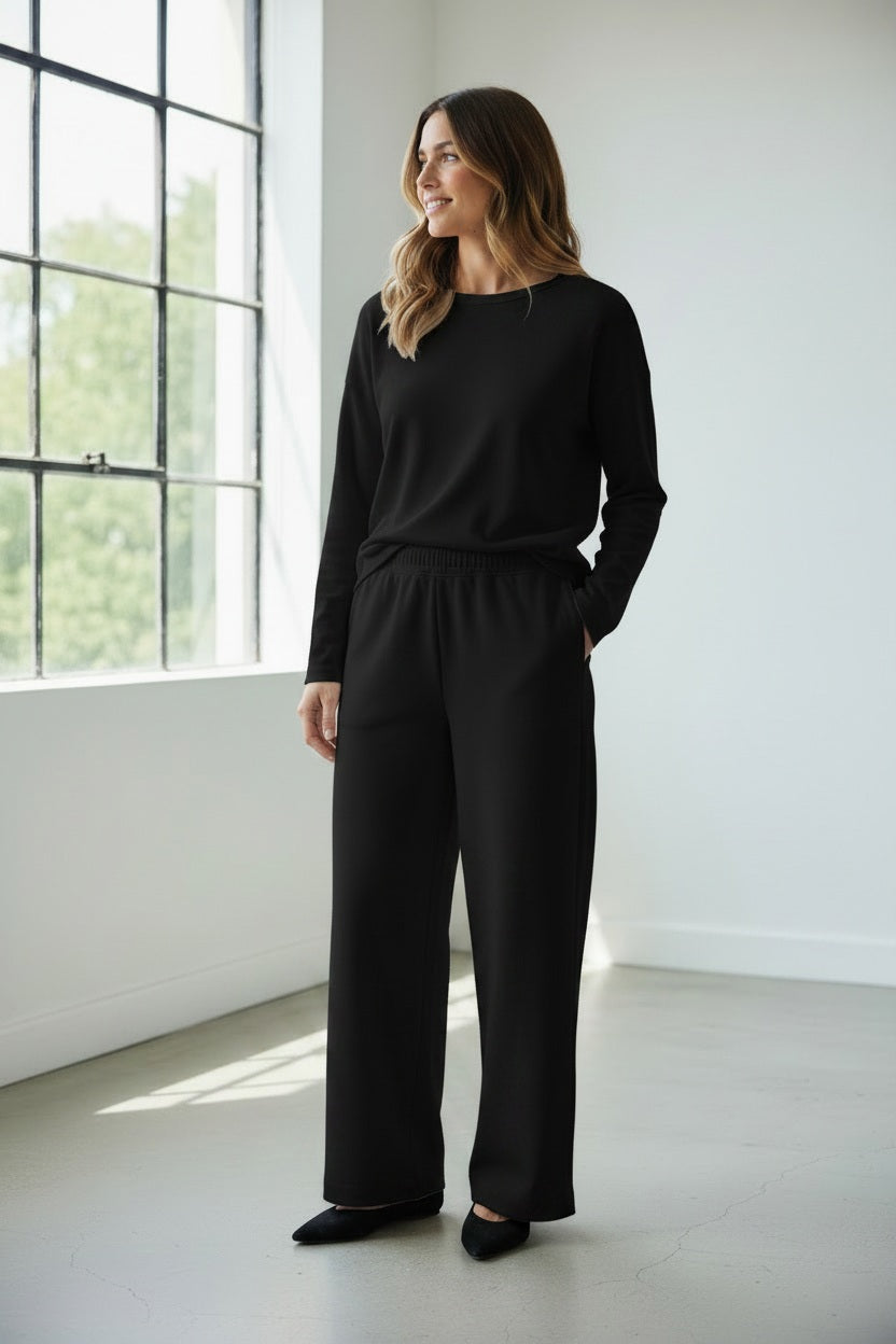 A person wears MEIMEIJ - PULL ON PANTS, featuring a wide-leg silhouette and elastic waistband, standing on a beige carpet in black shoes. These chic MEIMEIJ pants are made in Italy; the upper body is mostly out of frame.