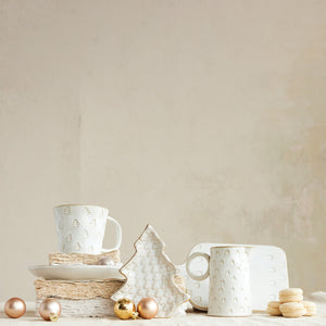 Creative Co-op DEBOSSED STONEWARE MUG WITH GOLD RIM AND TREE, matching creamer, and tree-shaped plate, all featuring a debossed tree pattern and gold rims, displayed with Christmas ornaments and small cookies as festive holiday drinkware.