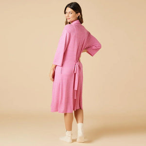 A woman wears a SOFTIES - DREAM SHAWL COLLAR ROBE IN FUSCHIA STRIPE over a matching tank top and drawstring shorts, offering spa-like luxury.