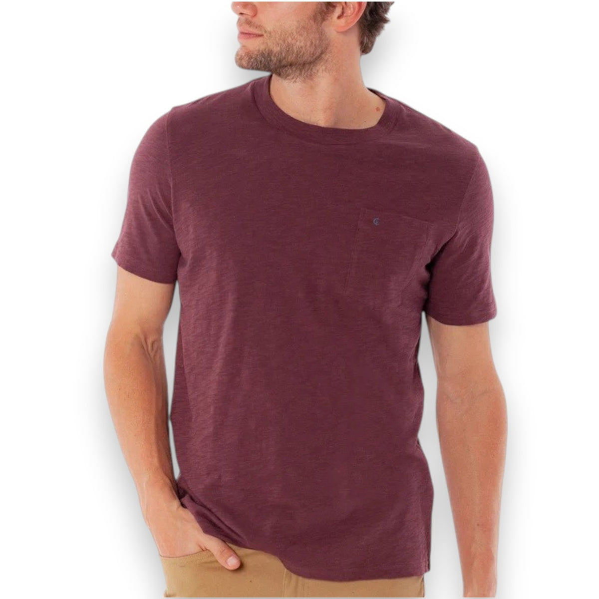 A person wearing the CRIQUET Slub Cotton Short Sleeve Pocket T-Shirt in Jam Band, featuring a small chest pocket and a subtle blue logo. The blurred greenery and wood background perfectly complement this vintage-inspired CRIQUET shirt, creating an effortlessly classic look.