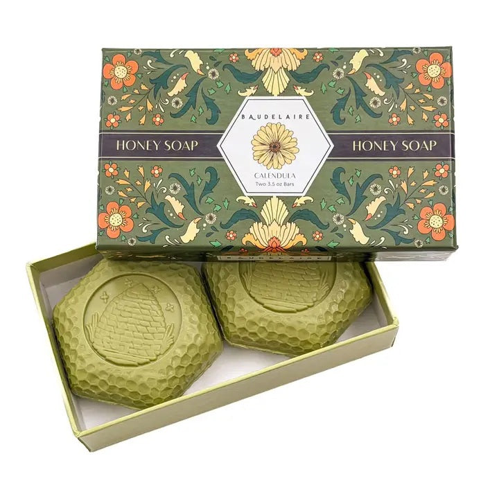 A beautifully packaged BAUDELAIRE Calendula Honey Soap Gift Box includes two 3.5 oz hexagonal green bars with an embossed beehive motif, partially displayed from a decorative floral box labeled “Calendula.” This elegant BAUDELAIRE gift set features triple-milled soap for a luxurious and gentle cleansing experience.