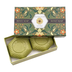 A beautifully packaged BAUDELAIRE Calendula Honey Soap Gift Box includes two 3.5 oz hexagonal green bars with an embossed beehive motif, partially displayed from a decorative floral box labeled “Calendula.” This elegant BAUDELAIRE gift set features triple-milled soap for a luxurious and gentle cleansing experience.