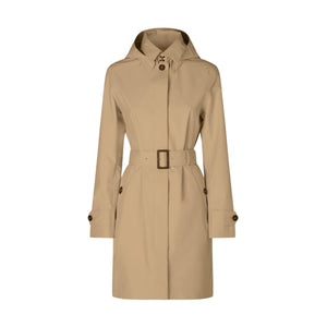 Wearing the SAVE THE DUCK - JACKIE RAINCOAT, made from recycled polyester with a belted trench design and hood up, a person stands indoors by a large window, gazing to the side with a neutral expression.