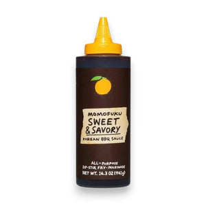 Two bottles of MOMOFUKU - SWEET & SAVORY KOREAN BBQ SAUCE by MOMOFUKU, each 16.3 oz, with yellow caps, dark labels, and an orange fruit logo. This all-purpose sauce offers a savory-sweet flavor that’s perfect for use as a dip, stir-fry ingredient, or galbi marinade.