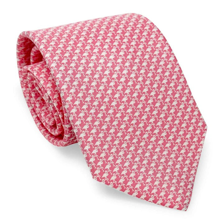 Close-up of the BIRD DOG BAY PETER-BLAIR Flamingo Silhouette Printed Silk Tie in pink, handmade in New York. Features a repeating white flamingo pattern and a pointed end, with the design visible across the tie.