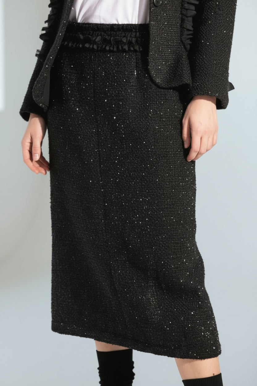 A woman wears the MEIMEIJ LUREX TWEED SKIRT with a black textured ruffle blazer, a white tee with black text, and black shoes with matching socks, posed against a white background.