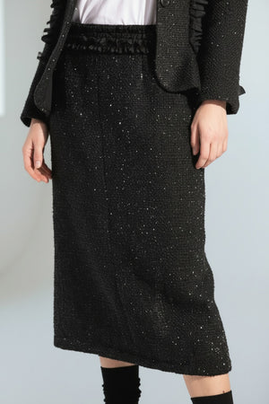 A woman wears the MEIMEIJ LUREX TWEED SKIRT with a black textured ruffle blazer, a white tee with black text, and black shoes with matching socks, posed against a white background.